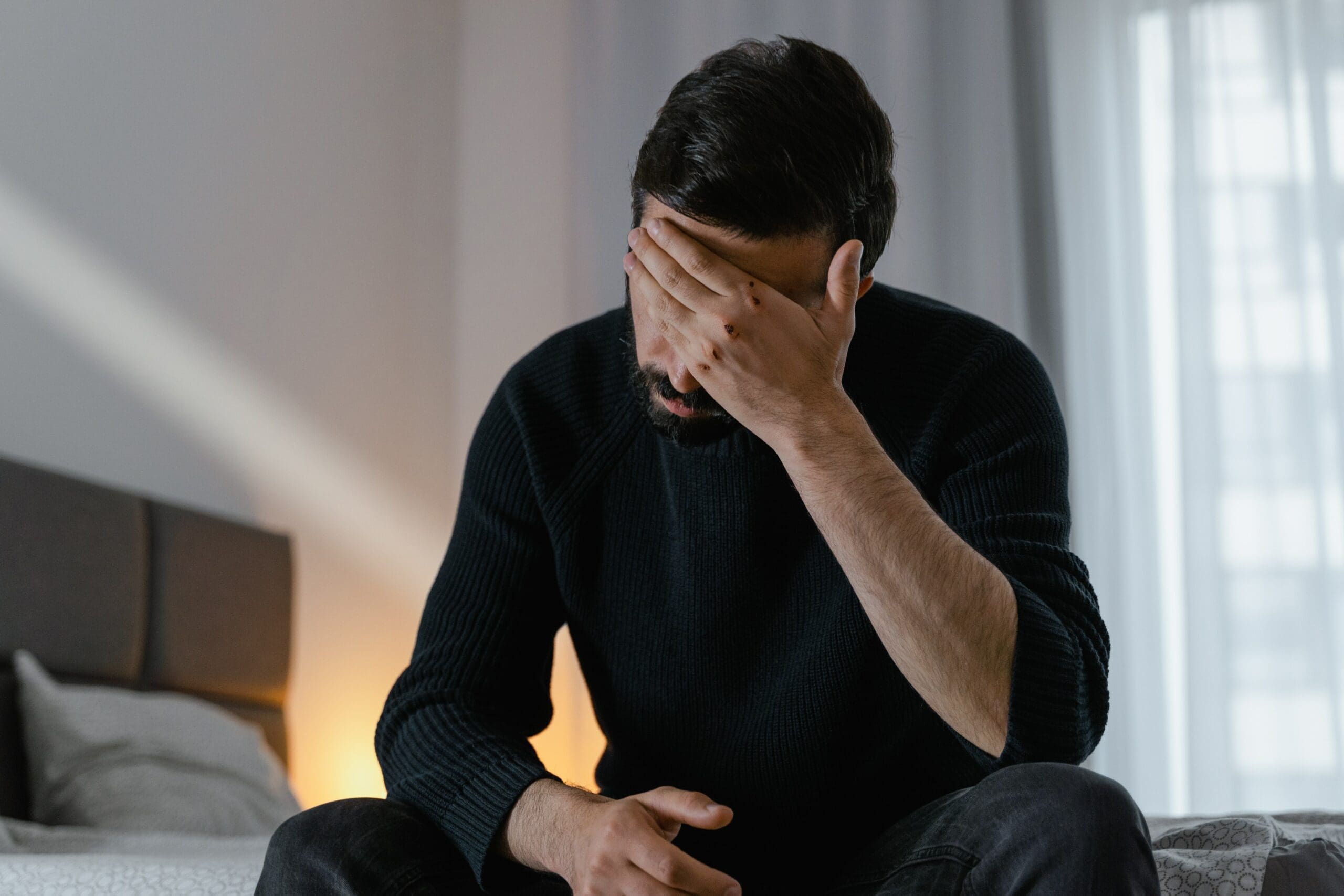 Frustrated Homeowners Man With Palm on Forehead Sitting on Bed